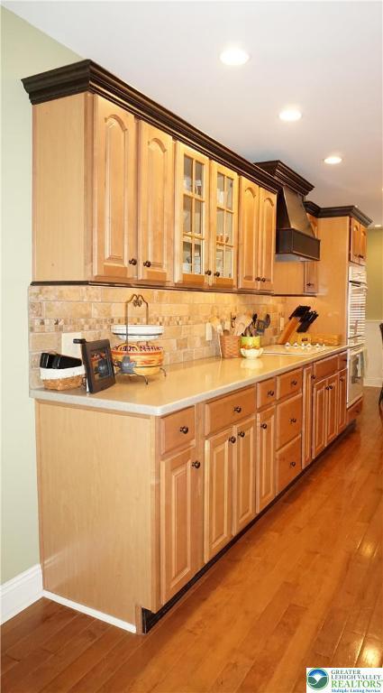 kitchen with custom range hood, light wood finished floors, double wall oven, baseboards, and recessed lighting