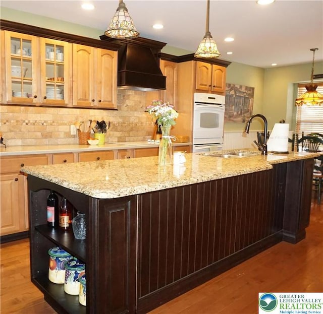 kitchen featuring white appliances, open shelves, premium range hood, wood finished floors, and a kitchen island with sink