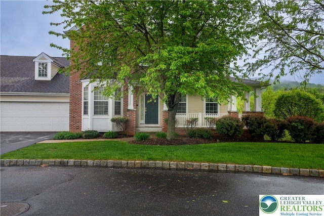 view of property hidden behind natural elements featuring asphalt driveway, a garage, brick siding, a front lawn, and covered porch