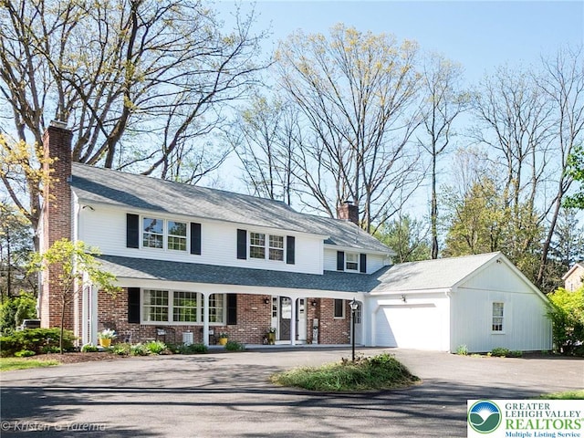 traditional-style home featuring asphalt driveway, a garage, brick siding, and a chimney