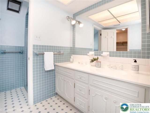 bathroom with tile walls, vanity, wainscoting, tile patterned floors, and tiled shower