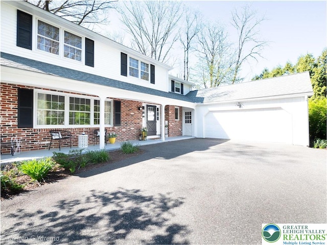traditional-style home featuring brick siding, an attached garage, driveway, and a shingled roof