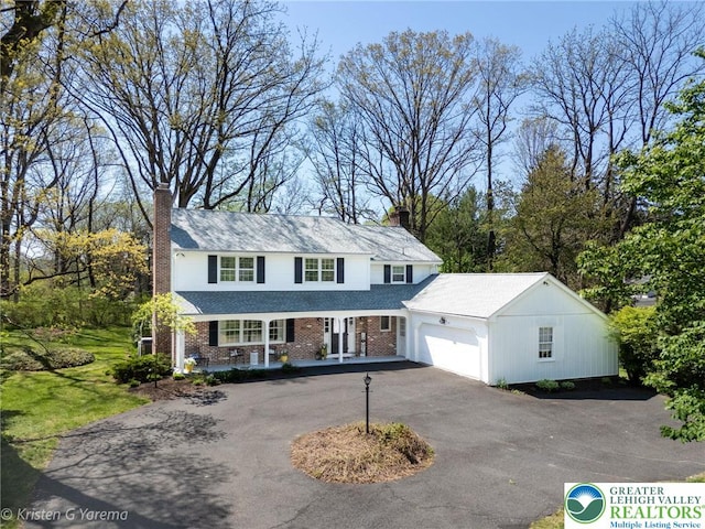 traditional home featuring a chimney, covered porch, an attached garage, and asphalt driveway