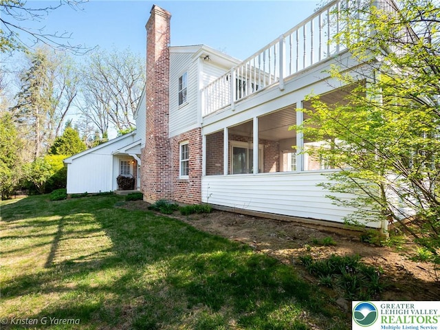 view of side of home featuring brick siding, a chimney, a yard, and a balcony