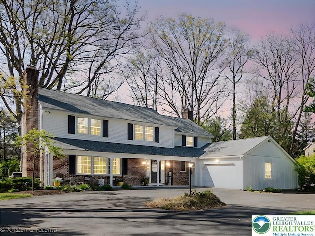 traditional-style home with asphalt driveway, a chimney, a garage, brick siding, and covered porch