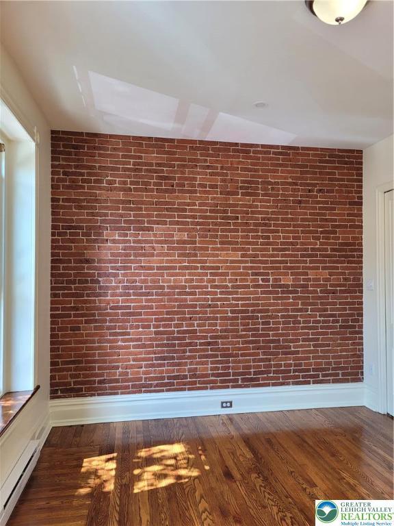 spare room with brick wall, wood finished floors, and baseboards