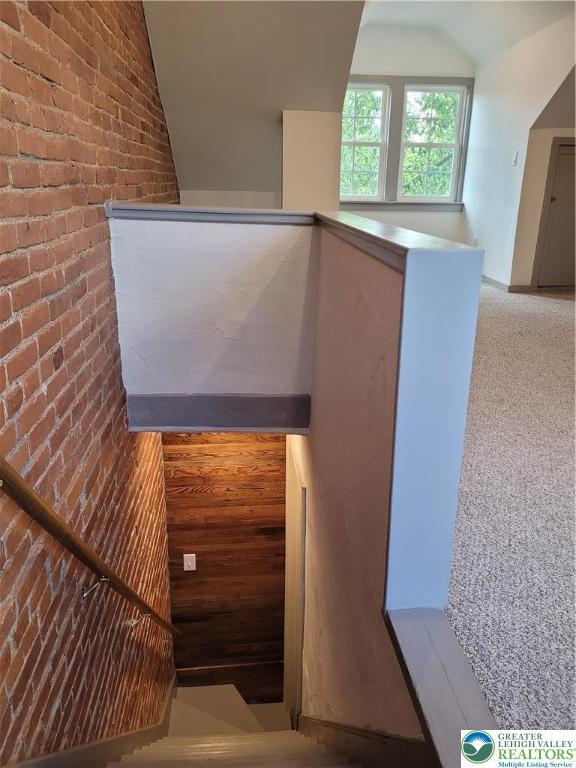 staircase with lofted ceiling, brick wall, and carpet