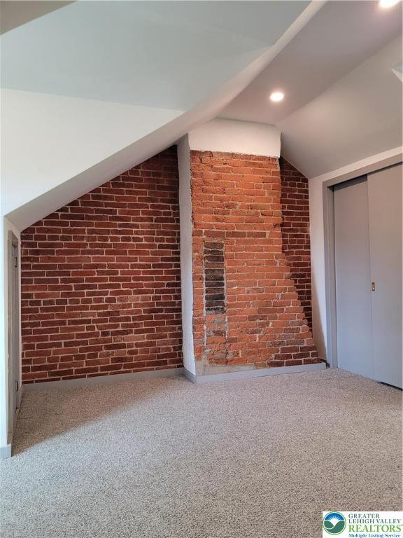 additional living space with brick wall, lofted ceiling, recessed lighting, and carpet flooring