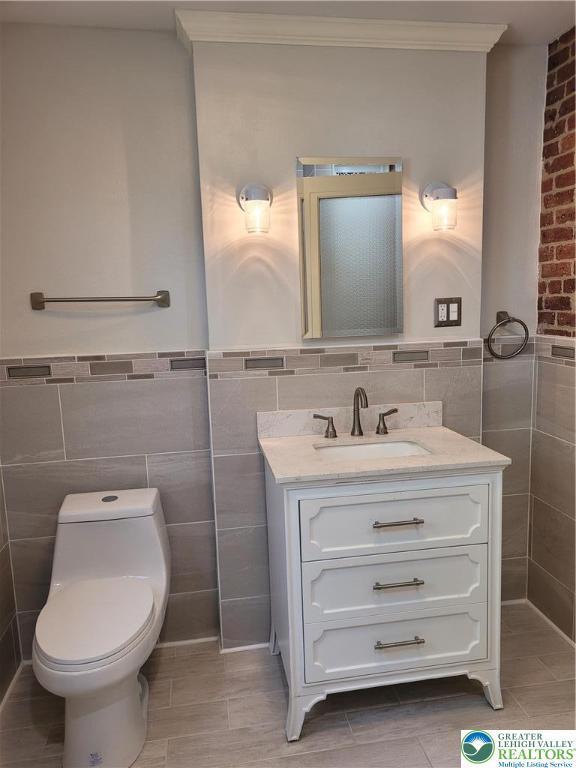 bathroom with tile walls, vanity, toilet, tile patterned floors, and wainscoting