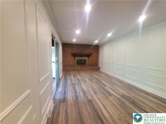 unfurnished living room featuring a decorative wall, a brick fireplace, wood finished floors, and crown molding