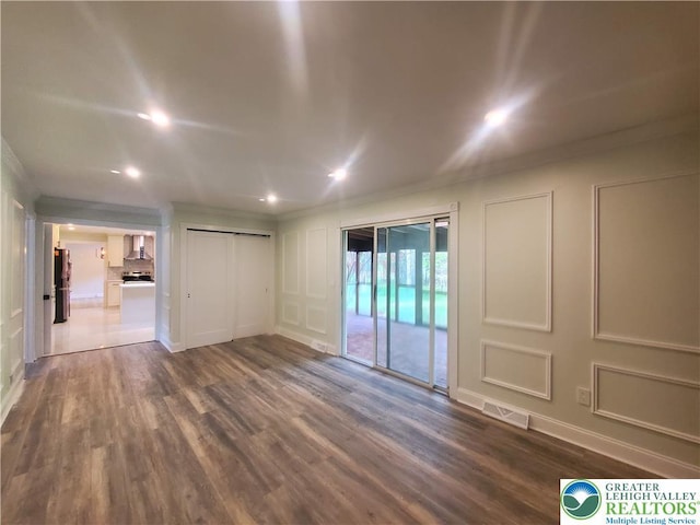 unfurnished room featuring a decorative wall, ornamental molding, dark wood-style floors, recessed lighting, and baseboards