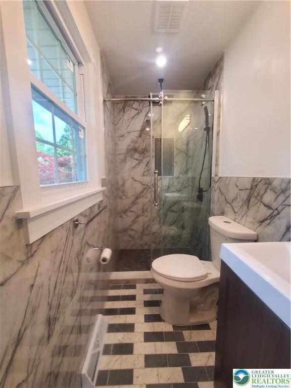 bathroom featuring tile walls, toilet, a marble finish shower, and vanity