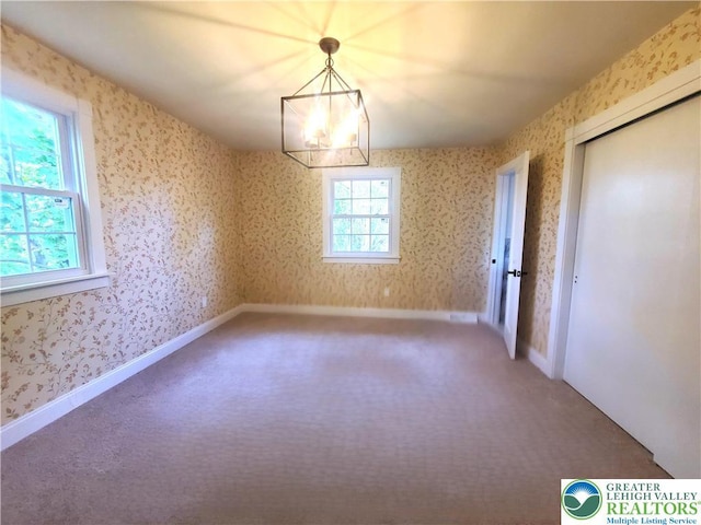 carpeted empty room featuring a chandelier and wallpapered walls