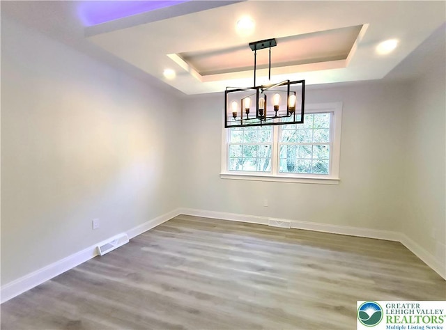 unfurnished dining area featuring a raised ceiling, wood finished floors, baseboards, and a chandelier
