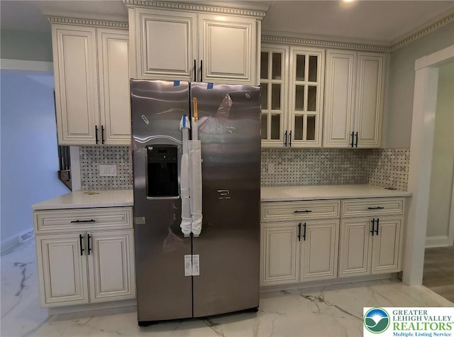 kitchen with stainless steel refrigerator with ice dispenser, light marble finish flooring, light countertops, backsplash, and glass insert cabinets