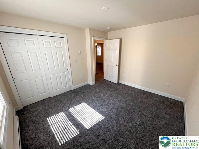 unfurnished bedroom with dark carpet, baseboards, and a closet