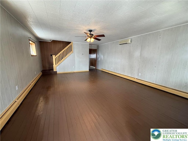 unfurnished living room featuring an AC wall unit, a ceiling fan, stairs, a baseboard radiator, and hardwood / wood-style floors