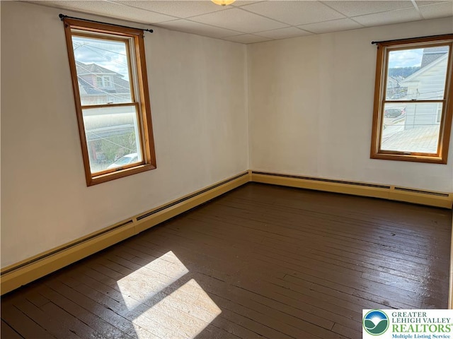 empty room with wood-type flooring, baseboard heating, and a drop ceiling
