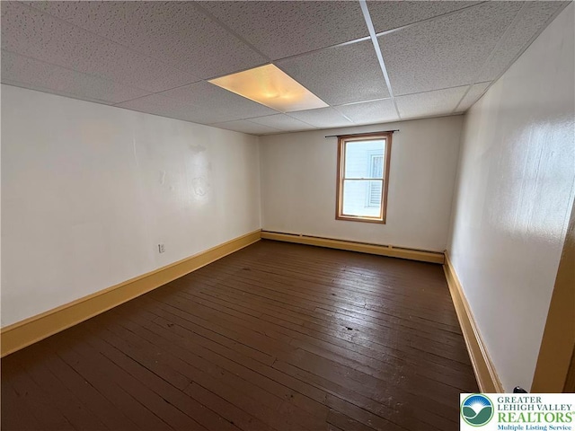 spare room with a baseboard radiator, a drop ceiling, baseboards, and dark wood-style floors