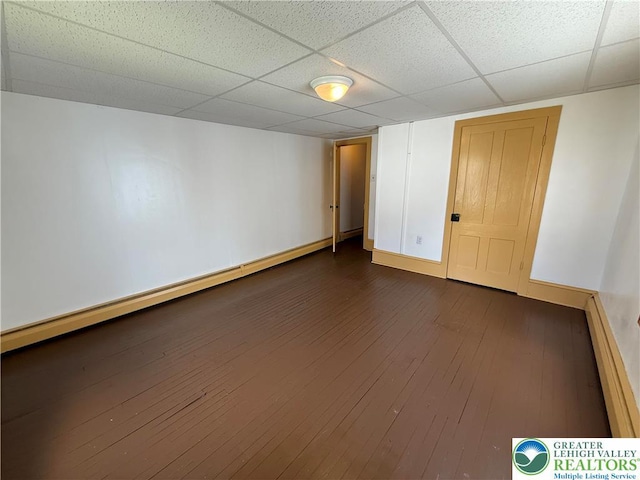 empty room featuring a drop ceiling, dark wood-type flooring, baseboards, and a baseboard heating unit