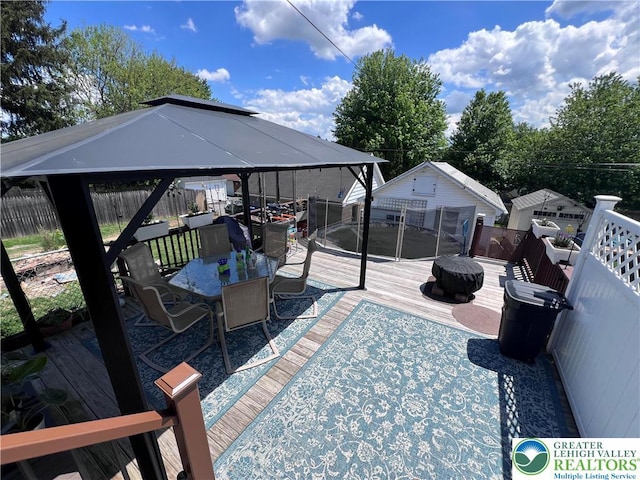 wooden terrace with a gazebo, fence, outdoor dining area, and an outdoor structure