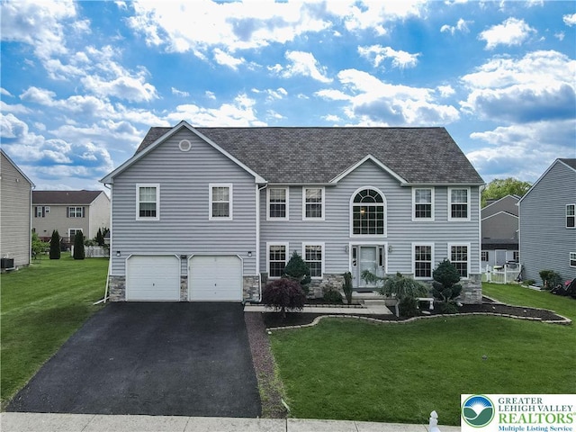 colonial-style house with stone siding, an attached garage, asphalt driveway, a front lawn, and roof with shingles