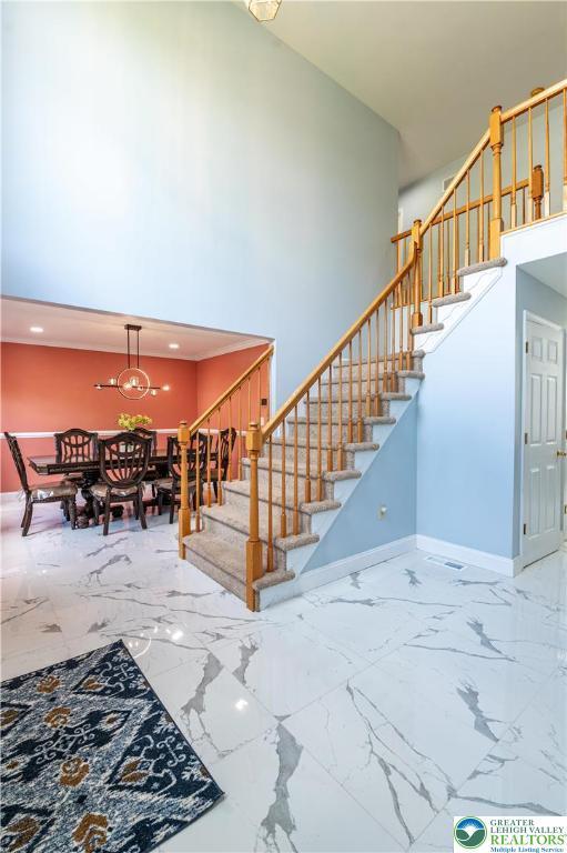 staircase with a high ceiling, baseboards, marble finish floors, and a chandelier