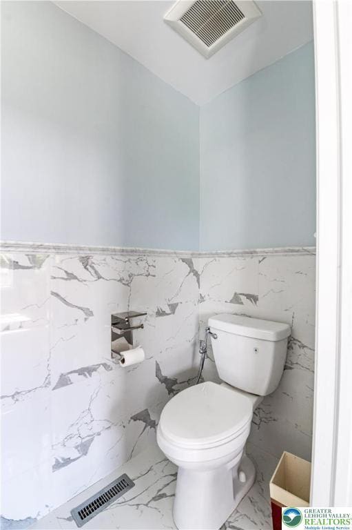 bathroom with wainscoting, toilet, and marble finish floors