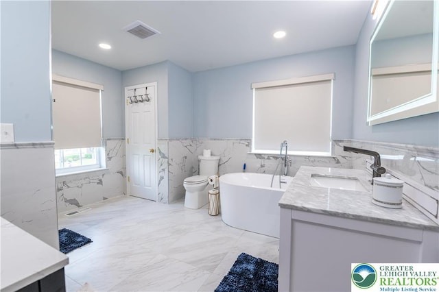full bath featuring tile walls, a freestanding bath, wainscoting, marble finish floors, and vanity