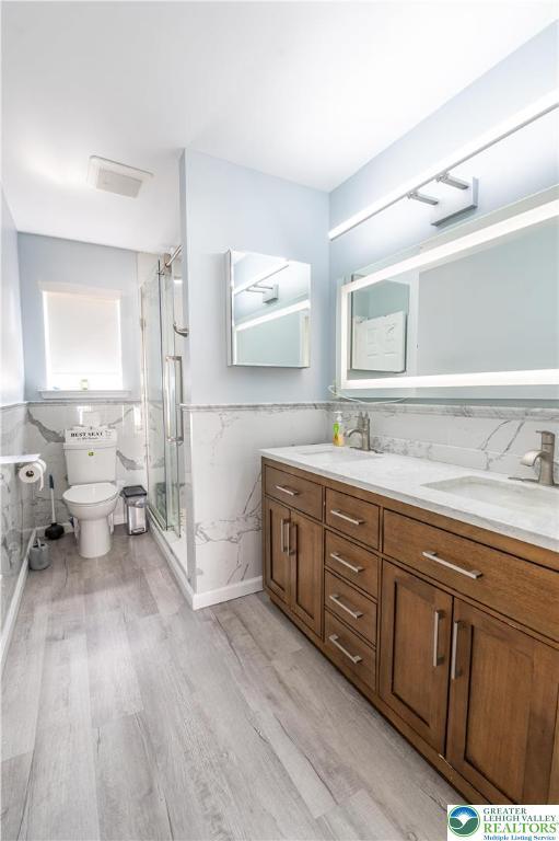 full bath featuring tile walls, toilet, wood finished floors, wainscoting, and a shower stall