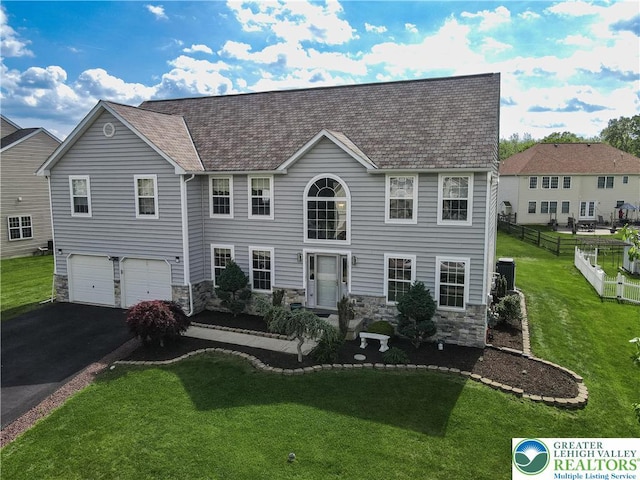colonial house featuring stone siding, driveway, and an attached garage