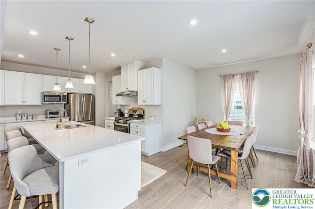 kitchen with appliances with stainless steel finishes, a sink, light wood finished floors, a kitchen bar, and baseboards