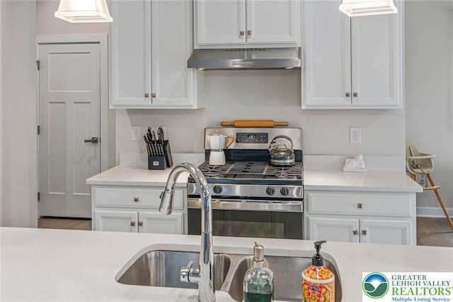kitchen featuring under cabinet range hood, stainless steel range with gas cooktop, white cabinets, and light countertops