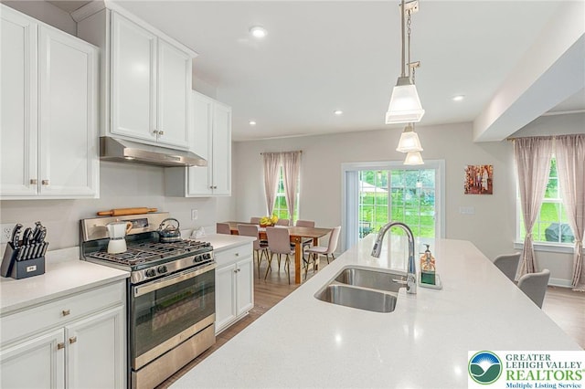 kitchen with stainless steel gas stove, under cabinet range hood, a sink, light countertops, and light wood-style flooring