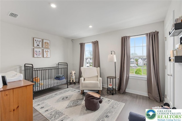 bedroom featuring light wood-type flooring, baseboards, a crib, and recessed lighting