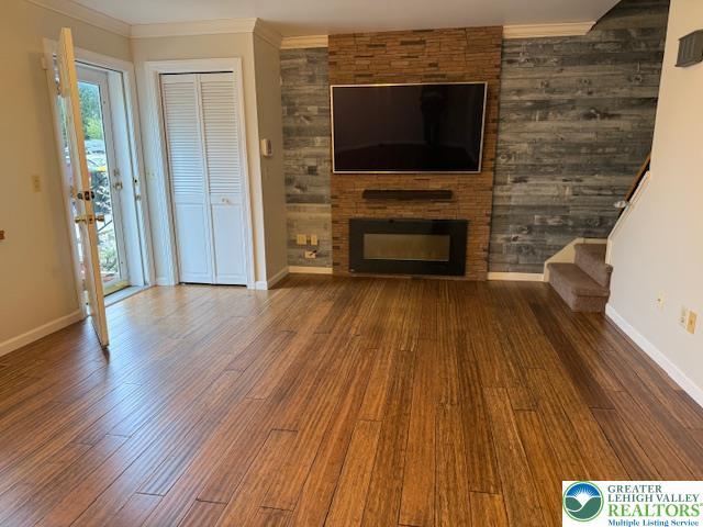 unfurnished living room featuring wood finished floors, a fireplace, baseboards, and crown molding