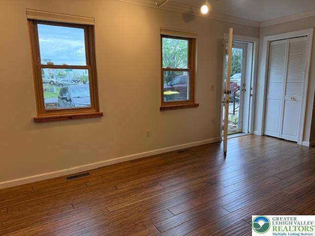 empty room with crown molding, baseboards, and dark wood-type flooring