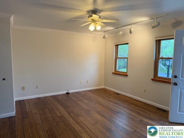 empty room with track lighting, a ceiling fan, wood finished floors, ornamental molding, and baseboards