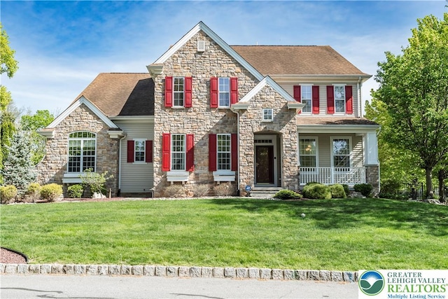 view of front of home with stone siding, a front yard, covered porch, and roof with shingles