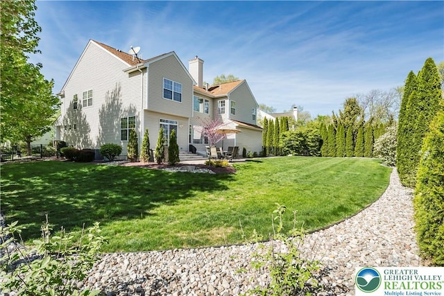 back of property featuring a patio area, a yard, and a chimney