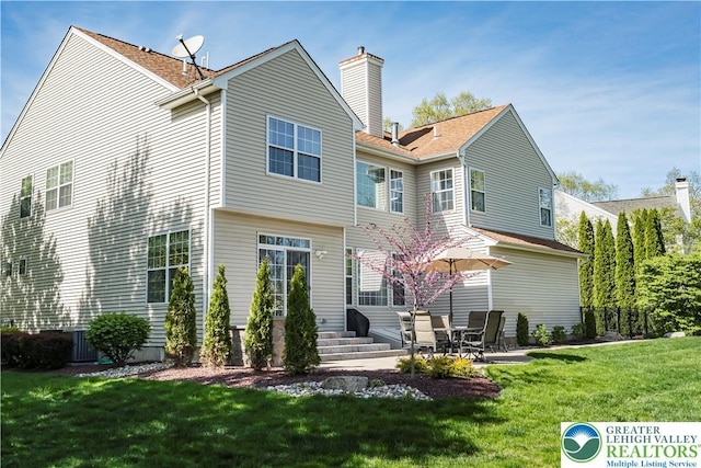 back of property with a chimney, a lawn, and a patio area