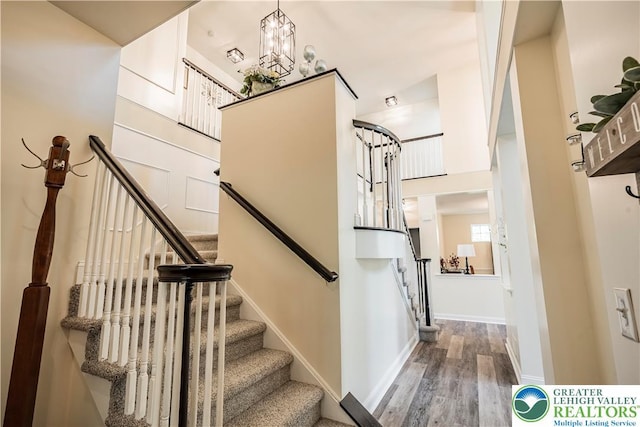 stairway with wood finished floors, baseboards, and a chandelier