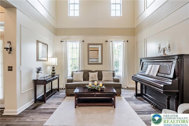 living area featuring a high ceiling, healthy amount of natural light, wood finished floors, and baseboards