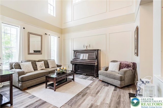 living area featuring healthy amount of natural light, light wood-style flooring, a high ceiling, and a decorative wall