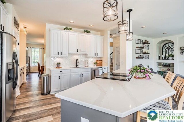kitchen featuring appliances with stainless steel finishes, light wood finished floors, a sink, a kitchen island, and pendant lighting