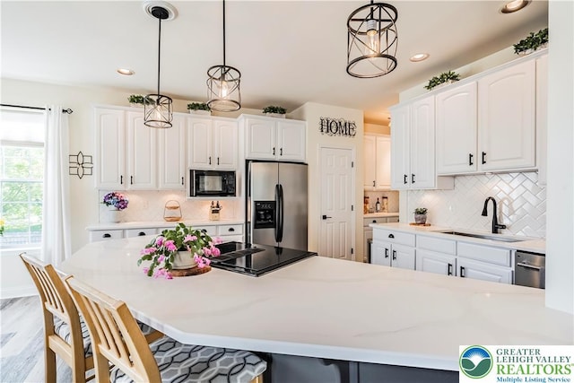 kitchen featuring black appliances, a sink, a breakfast bar area, hanging light fixtures, and white cabinets