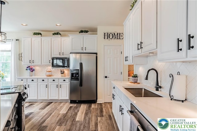 kitchen featuring stainless steel appliances, tasteful backsplash, a sink, white cabinets, and light wood-style floors