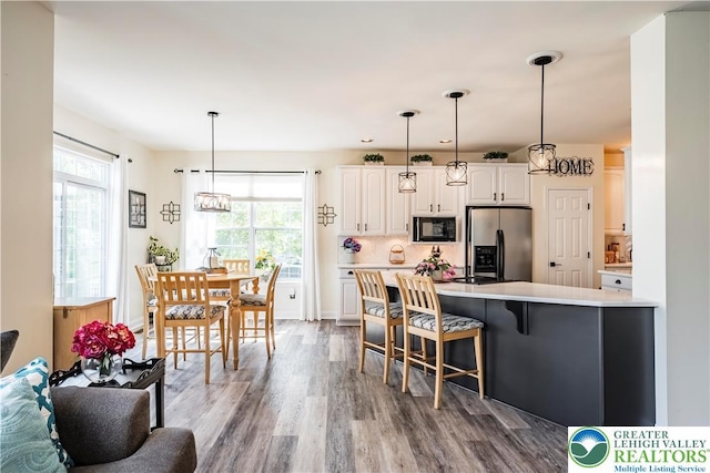 kitchen with stainless steel fridge, black microwave, dark wood finished floors, white cabinets, and healthy amount of natural light