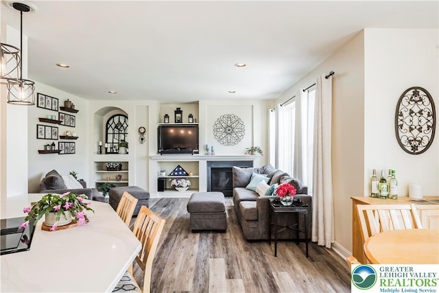 dining space with wood finished floors, a glass covered fireplace, built in shelves, and recessed lighting