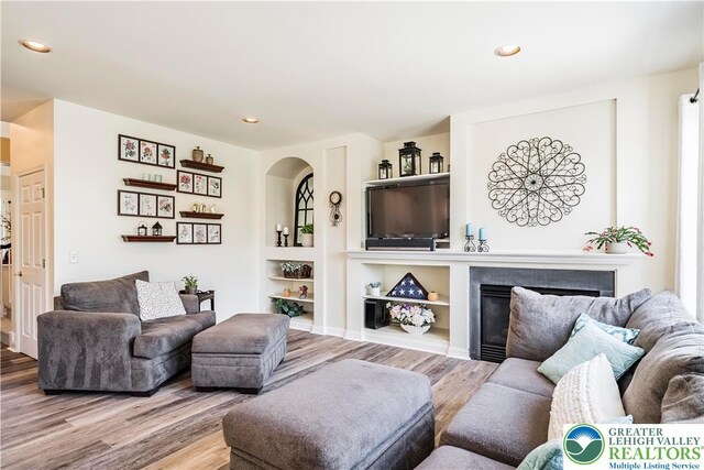 living area with wood finished floors, arched walkways, recessed lighting, a glass covered fireplace, and built in features